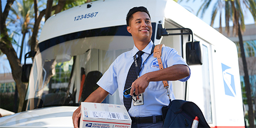USPS mail carrier scanning a Priority Mail box while standing in front of a Next Generation Delivery Vehicle (NGDV).