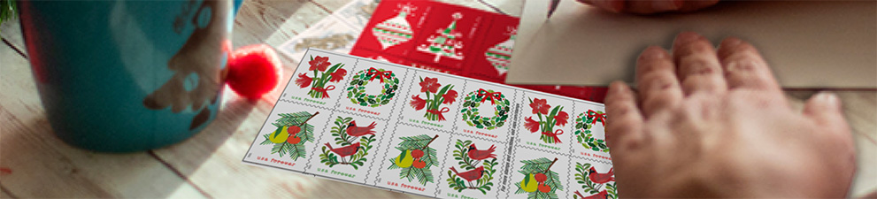 A person addressing a letter with First-Class Mail Forever® holiday stamps on the table.