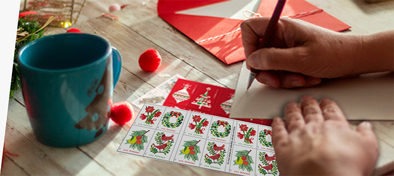 A person addressing a letter with First-Class Mail Forever® holiday stamps on the table.